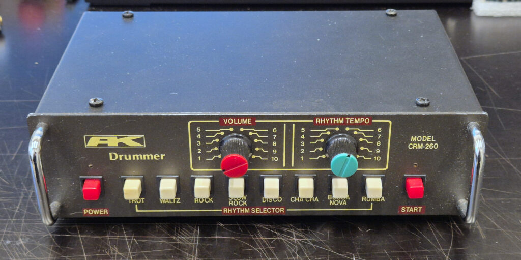 A picture of the front of the AK-Drummer CRM-260, visible are 8 rhythm selection buttons, a power button, a start/stop button and two knobs (volume and tempo)